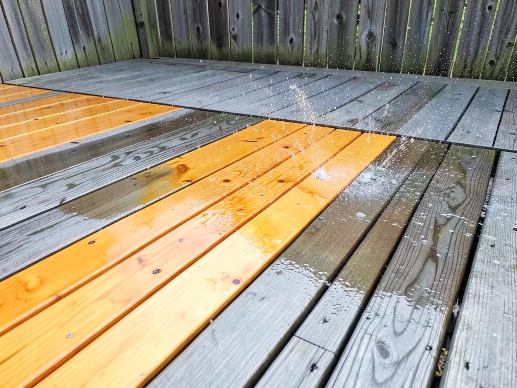 Wooden deck being pressure washed, clean bright boards next to weathered gray boards
